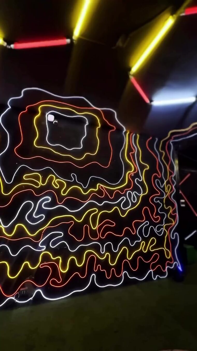 Parede preta com linhas orgânicas de neon branco, amarelo e vermelho